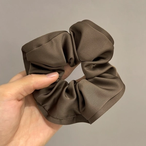 Detail of brown satin scrunchie with soft ruffled texture and silky reflective fabric
