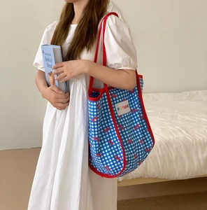 Detail of blue plaid tote bag with red handles shown in a lifestyle setting