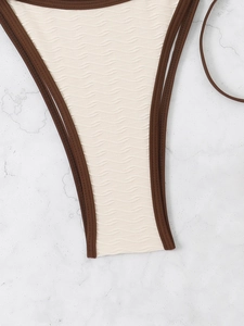 Close-up of cream triangle bikini bottom with brown piping and wave textured fabric