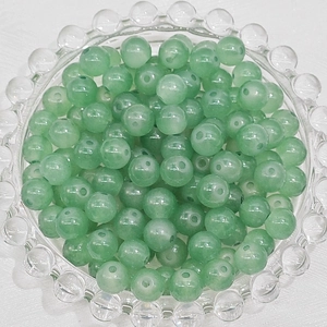 Detailed macro view of translucent green round glass beads stacked in a glass tray