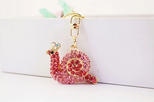 Close-up of pink crystal rhinestone snail keychain with golden lobster clasp detail