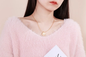 Close-up of golden Pisces zodiac shell pendant on snake chain worn by a female model