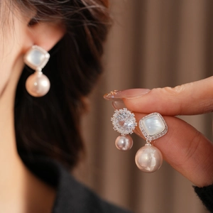 Close-up of square shell inlay and shimmering zircon detail on the pink pearl earrings