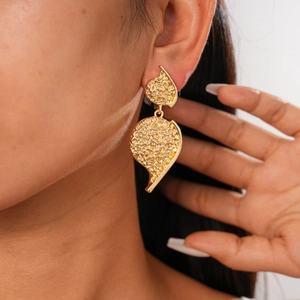 Detail of gold wrinkled heart earrings with irregular hammered leaf texture on model