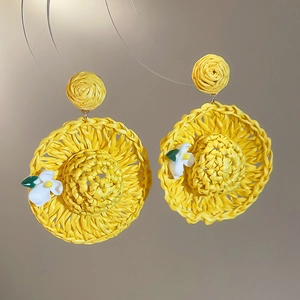 Detail of yellow raffia straw hat earrings with white flower accent and green leaf deco