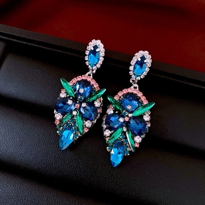 Macro shot of asymmetric crane earrings featuring colorful rhinestones and teardrop crystals