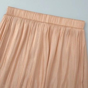 Detailed close-up of champagne pleated satin pants with elastic waist and glossy texture