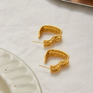 Detailed close-up of gold heart earrings with woven texture on soft white linen fabric