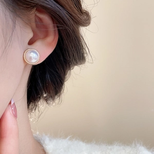 Close-up of pearl stud earrings with gold borders worn for an elegant daily look