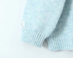 Close-up of light blue mohair knit sweater featuring ribbed cuffs and a decorative side label