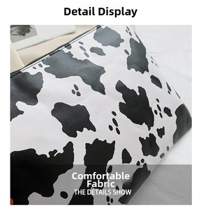 Detail shot of black and white cow print fabric with black top zipper on stylish clutch