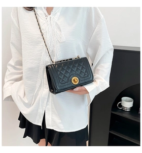 Detail of a black quilted crossbody bag with a gold twist lock and chain strap