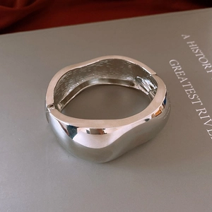 Vue détaillée du bracelet argenté ondulé montrant la surface polie et le fermoir charnière