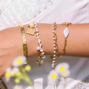 Détail de bracelets superposés plaqués or 18K avec gravure papillon et perles baroques