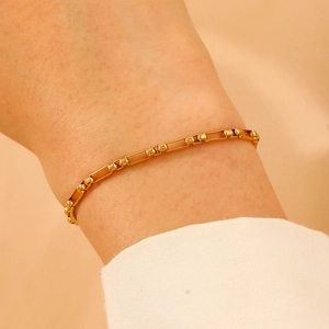 Detail of a gold link bracelet featuring alternating rectangular loops and small beads