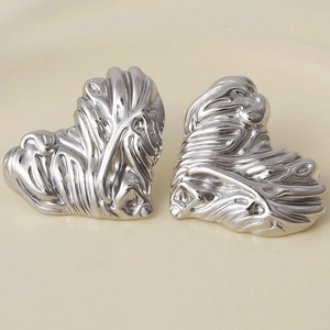 Macro shot of silver lava textured heart-shaped stainless steel earrings on beige background