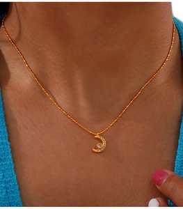 Detail of gold crescent moon pendant with crystals on a delicate beaded chain necklace