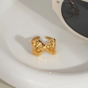 Détail d'une bague dorée aux formes organiques sur socle en céramique blanche brillante
