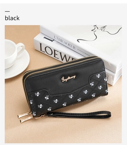 Detail of black leather long wallet with floral patterns and double zippers on a desk