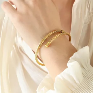 Minimalist gold twisted cable bypass bangle with spherical ends on female wrist