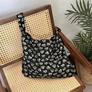 Detailed texture of black floral cotton tote bag with green heart prints on a rattan chair