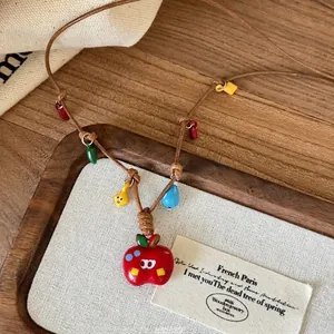 Handmade necklace with red enamel apple pendant and colorful beads on brown woven cord