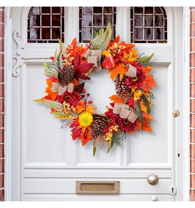 Detail of autumn wreath with red sunflowers, pine cones and pumpkins on a white door