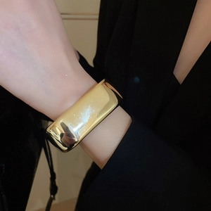 Polished gold wave wide cuff bracelet shown on wrist against a dark background
