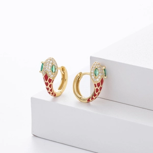 Detail of snake earrings in gold with red enamel texture and green gemstone eyes