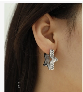 Close-up of star-shaped silver earrings with metallic strap texture on a female model
