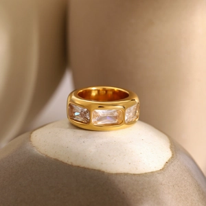 Macro view of wide gold band ring with three rectangular zircons on ceramic base