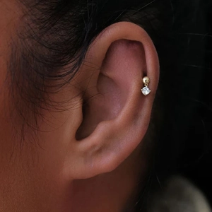 Detailed close-up of a gold star piercing stud with a round dangling diamond on the ear