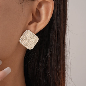 Close-up of a gold square stud earring with pave-set crystals on a model's ear