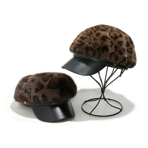 Leopard print faux mink baker boy hat with black leather brim on a metal stand