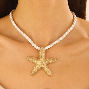 Detailed close-up of a large gold starfish pendant on a white chunky woven cord necklace