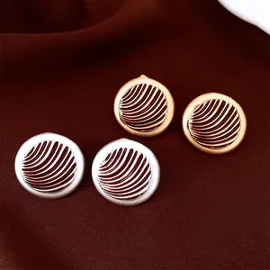 Matte gold and silver round stud earrings with concentric ripple texture on red velvet