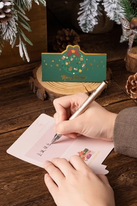 0.5mm gold pen with Merry Christmas cards on a wooden table with pine cones