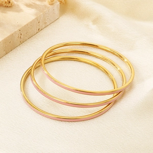 Detailed macro view of three stacked gold stainless steel bangles with pink enamel inlay