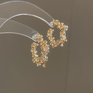 Detail of gold C-shaped hoop earrings with micro-pave crystal star shimmer finish