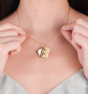 Detail of a gold envelope necklace with a pearl accent worn by a model on the collarbone