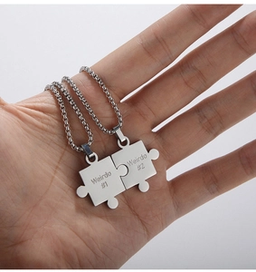 Detail of puzzle piece necklaces with Weirdo engraving held in palm for couples