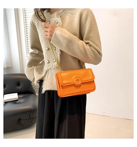 Detail of an orange crossbody bag featuring a round metal lock and golden chain strap