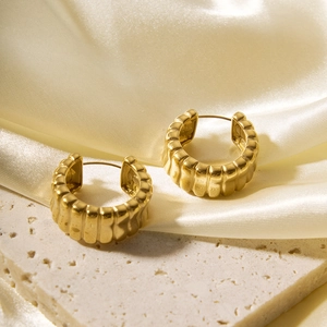 Detailed close-up of gold hollow earrings with hammered texture on a beige stone base