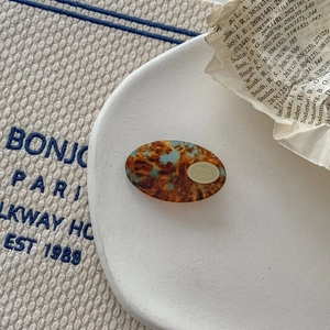 Detail of oval acetate hair clip with tortoiseshell pattern and gold brand logo tag