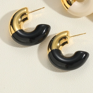 Macro shot of C-shaped gold-plated earrings with black oil-drop finish on textured surface