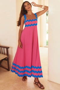 Detail of pink cotton maxi dress featuring blue scalloped trim on a sunlit terrace