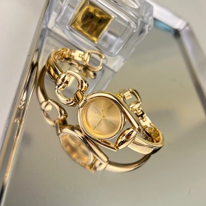 Elegant gold women's watch with metal chain strap on mirror surface near perfume bottle