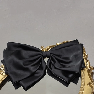 Close-up of a large black satin bow hair clip placed on a vintage gold framed mirror