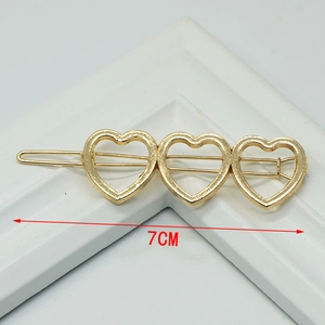Detail showing 7cm golden metallic hair clip with three hollow heart shapes on white stand