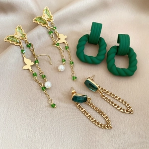 Detail of green acrylic and gold-plated earrings set on champagne silk fabric background